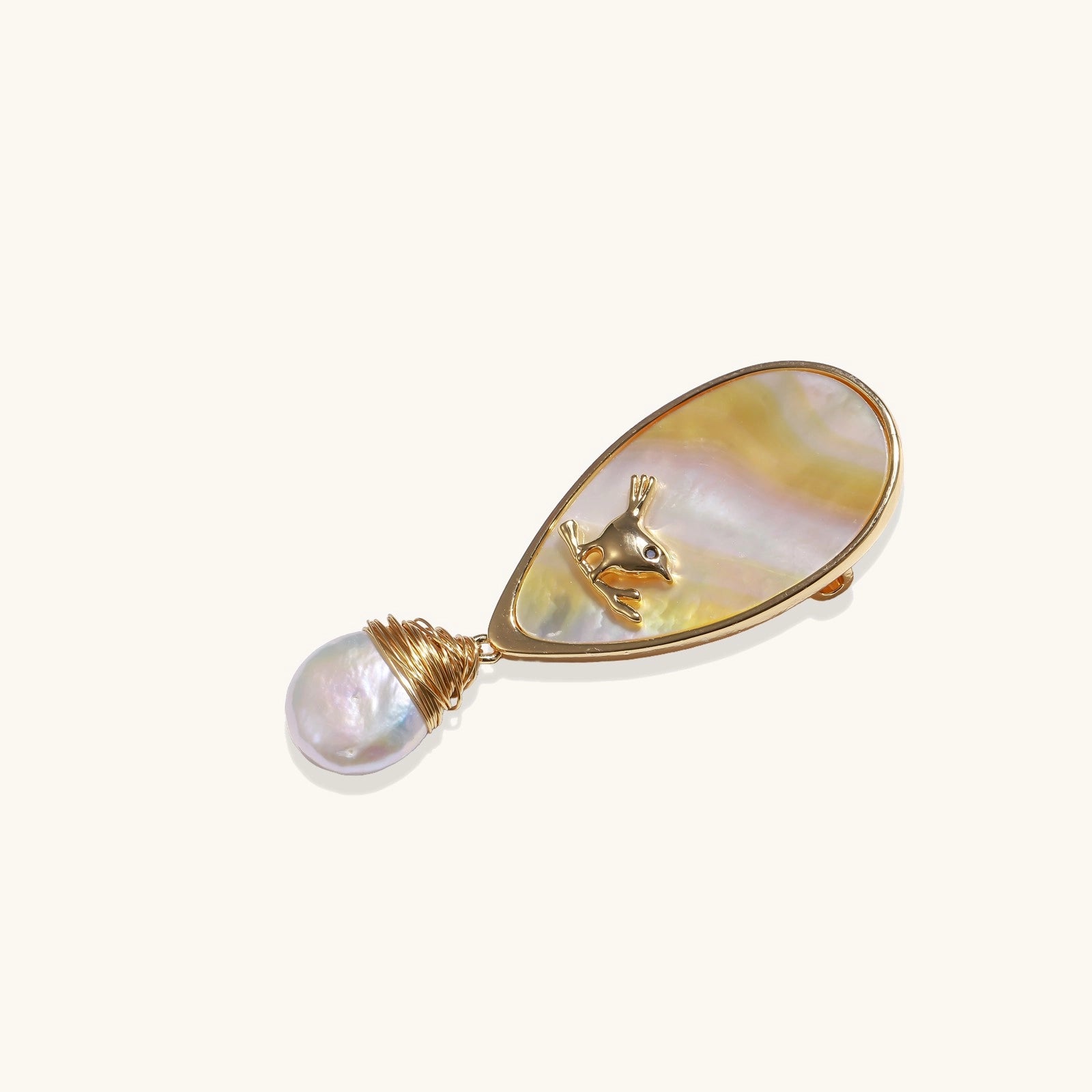 Teardrop-shaped pin with iridescent golden shell, small gold frog figure, and baroque pearl drop on white background.