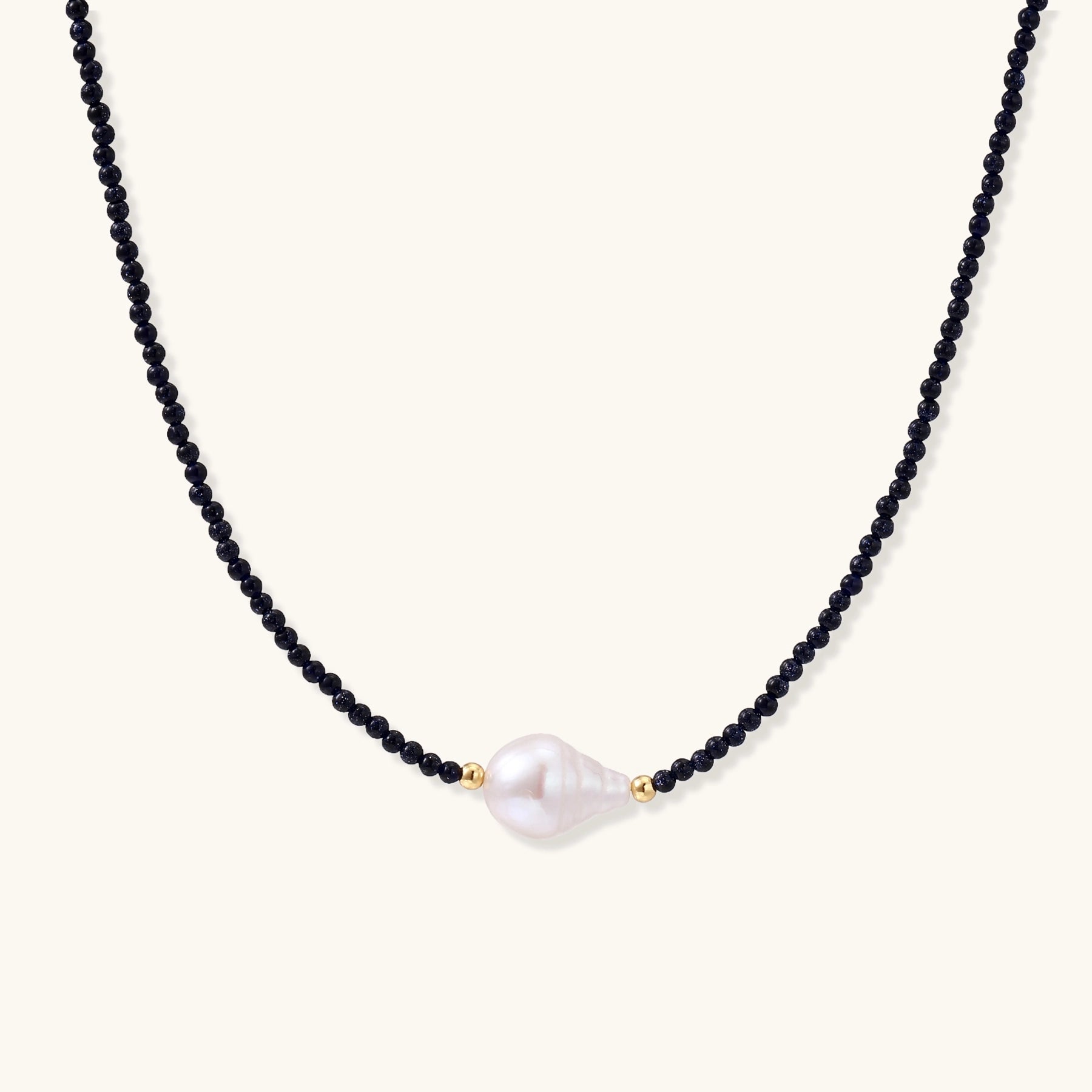 Elegant necklace with blue sandstone beads and baroque pearl centerpiece with gold accents on neutral background.