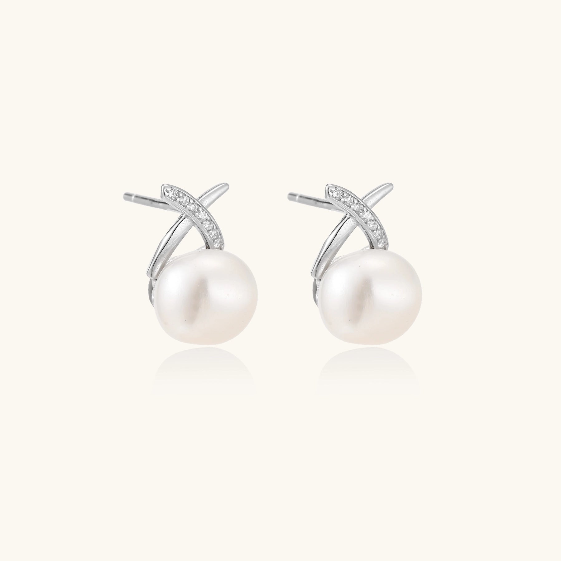 Sterling silver cross-shaped stud earrings with round freshwater pearls dangling below on white background.