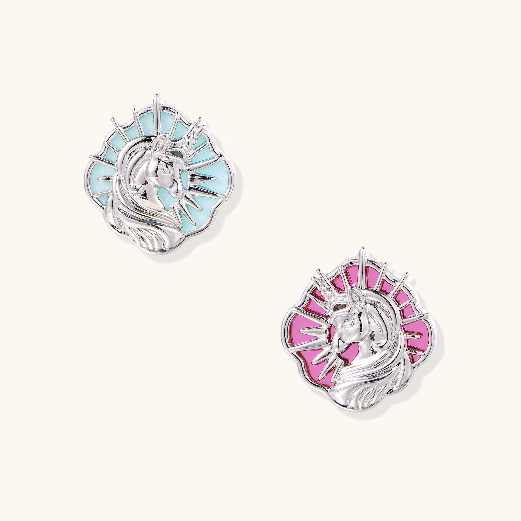 Two unicorn-shaped stud earrings with radiating spikes, one with turquoise stone and one with pink stone, on white background.