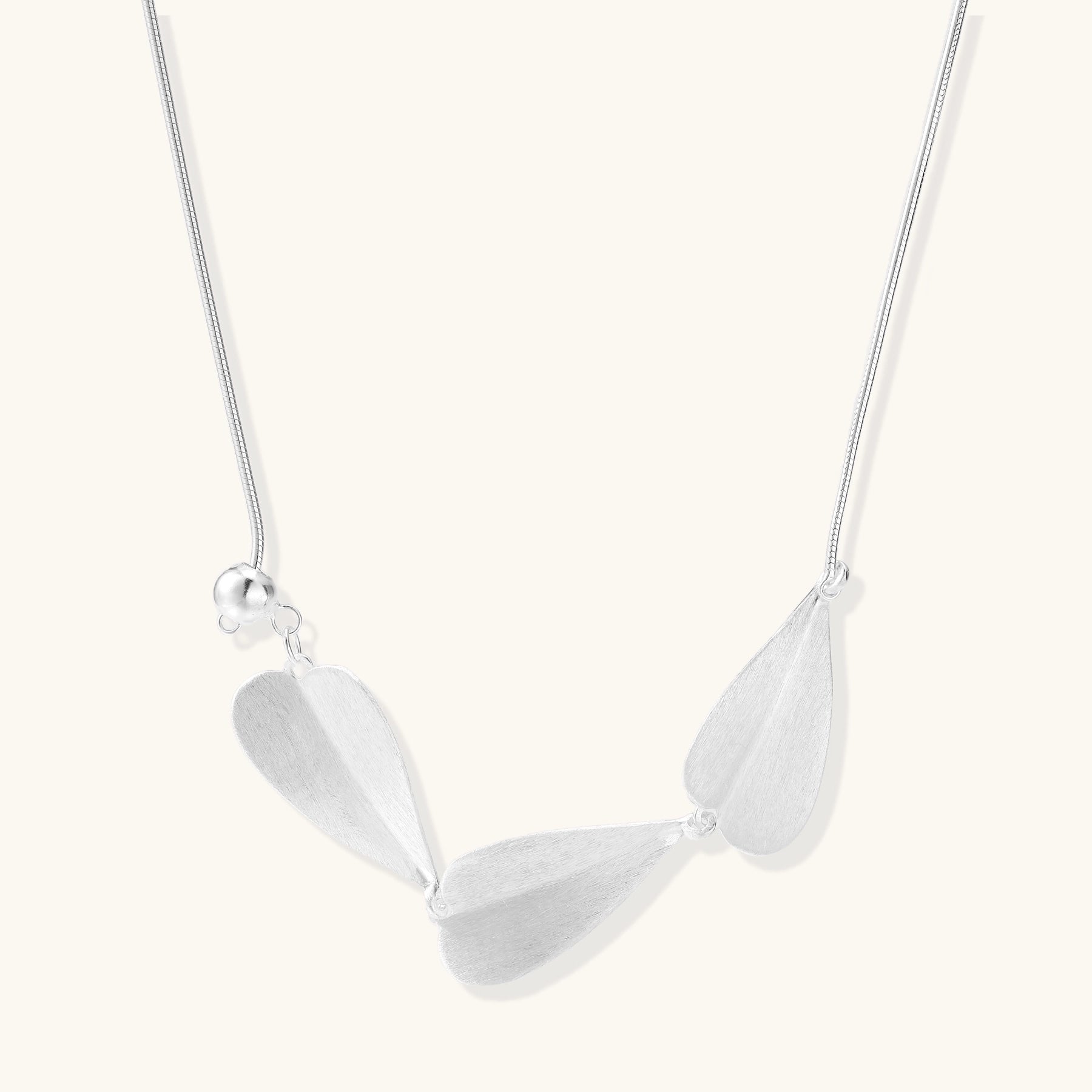 Delicate sterling silver necklace with brushed leaf pendants distributed along a fine chain on white background.