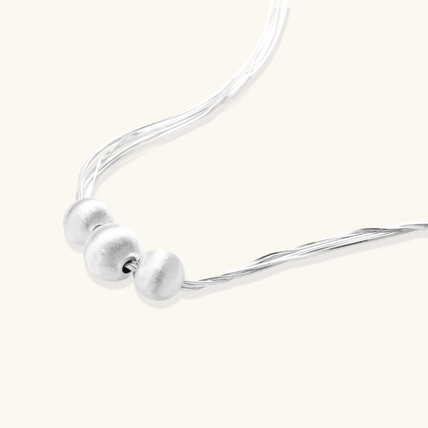 Multi-strand sterling silver necklace with three polished round beads clustered at center on white background.