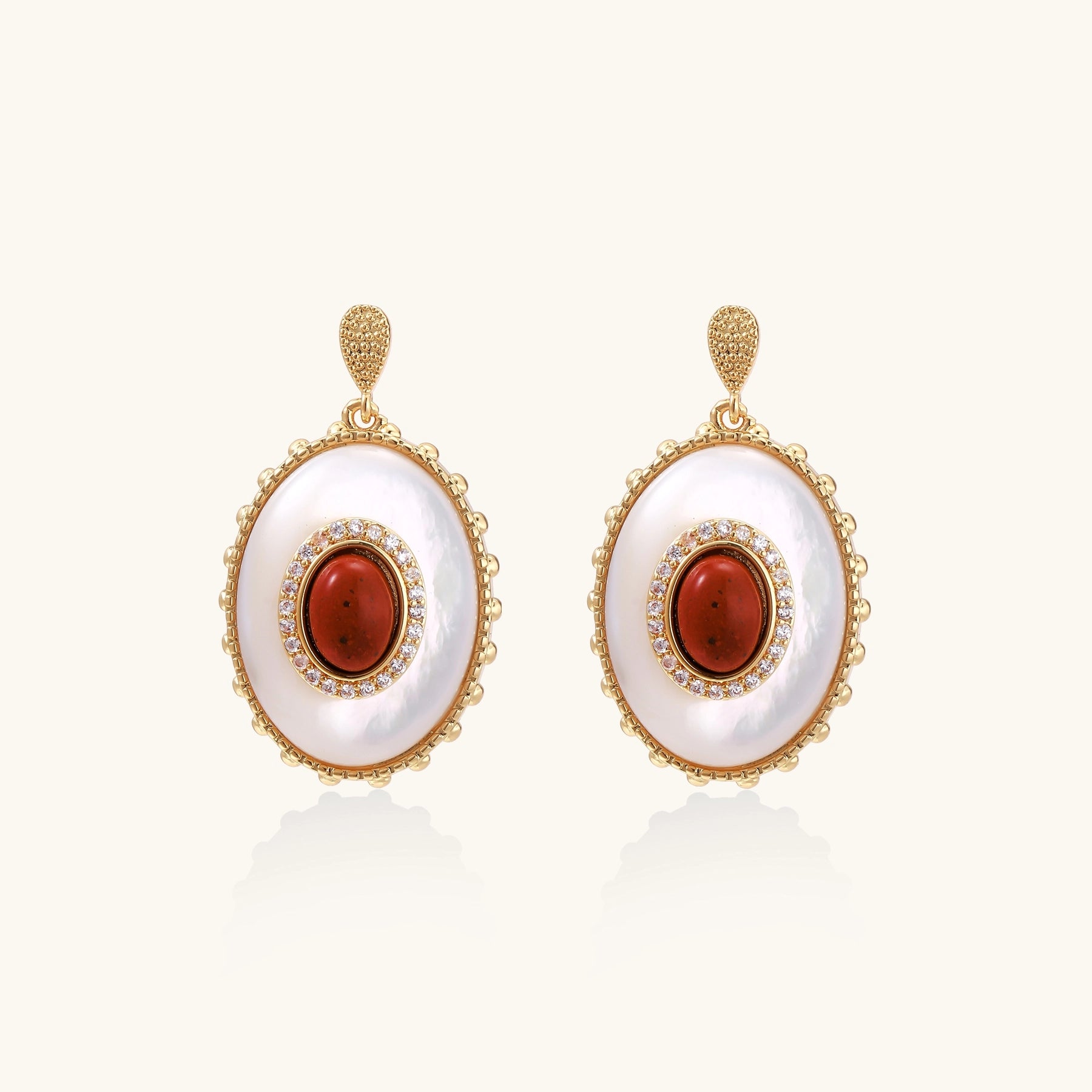 Gold-plated drop earrings with oval mother-of-pearl stones, central red gemstones, and crystal accents on white background.