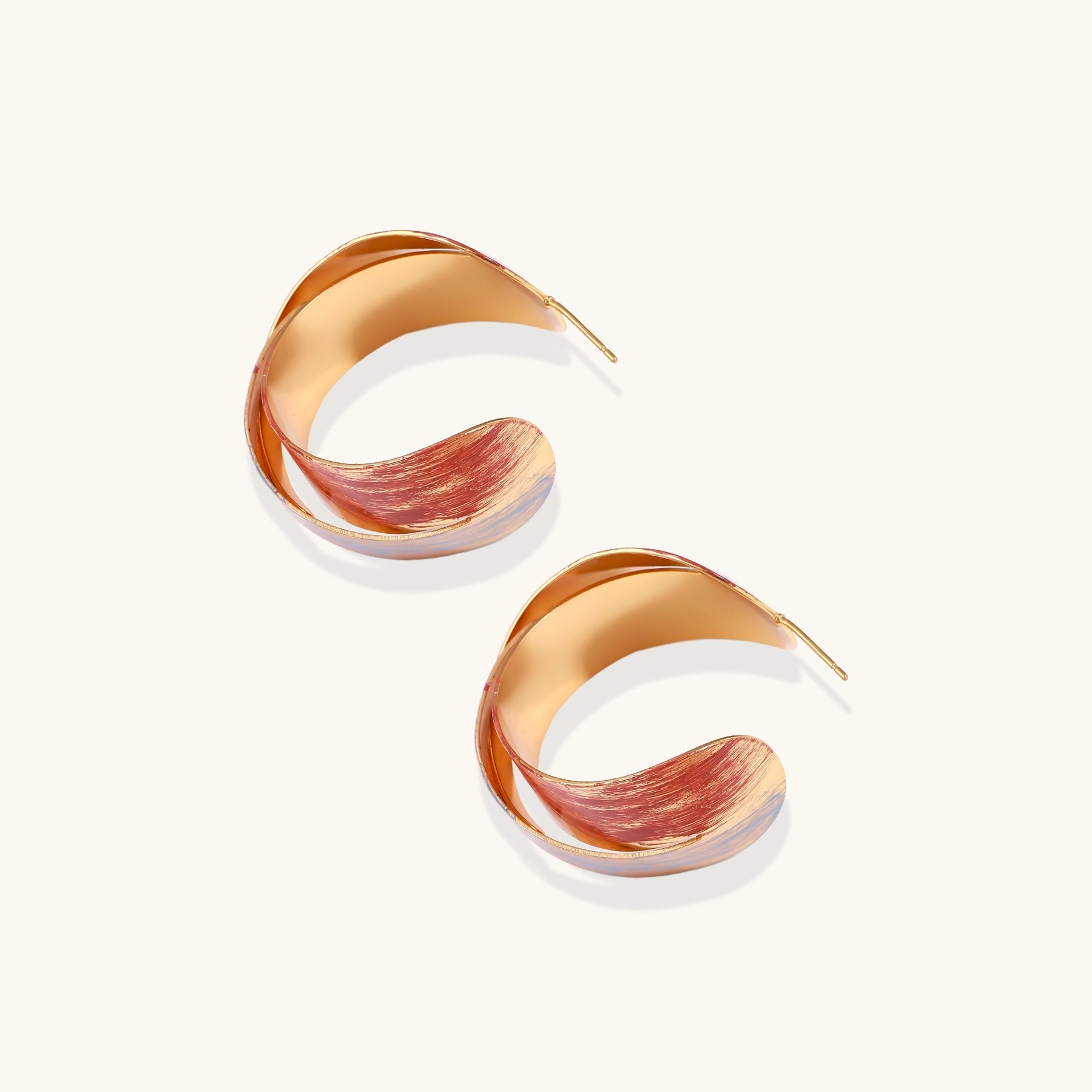 Twisted gold-plated brass earrings with multicolored enamel brushstroke patterns in burgundy and blue on white background.