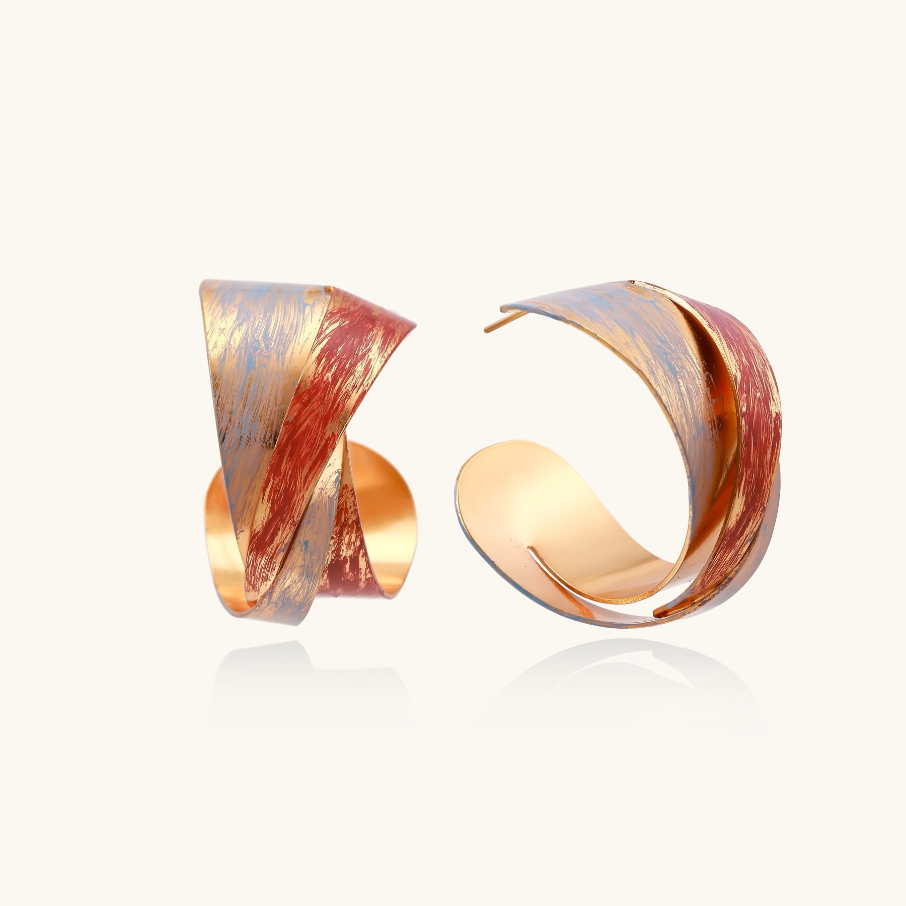 Twisted gold-plated brass earrings with multicolored enamel brushstroke patterns in burgundy and blue on white background.