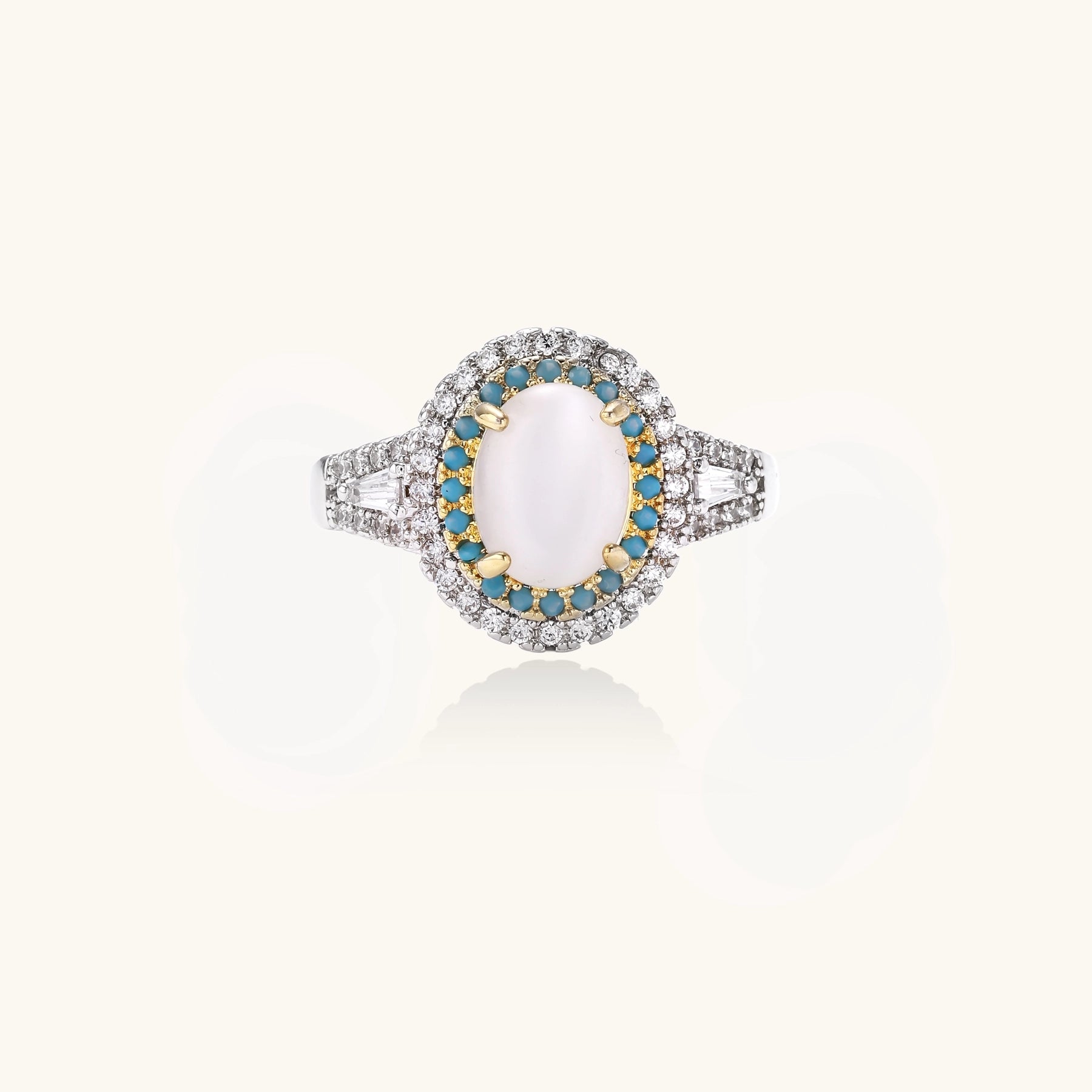 Gold-plated ring with oval cat's eye stone center, blue accent stones, and crystal halo on white background.