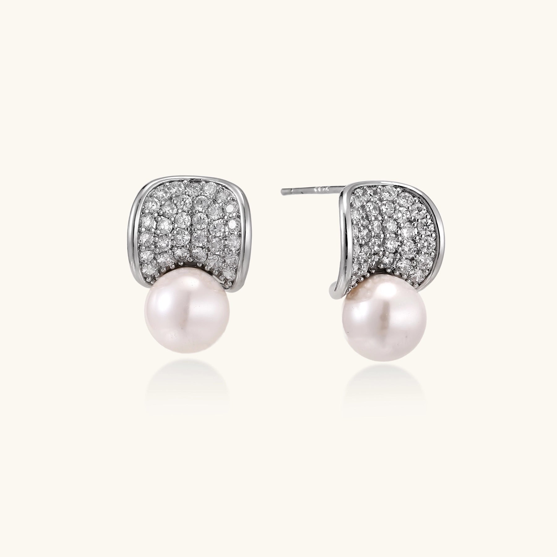 Elegant gold-plated curved earrings with diamond pavé crescents and suspended freshwater pearls on neutral background.