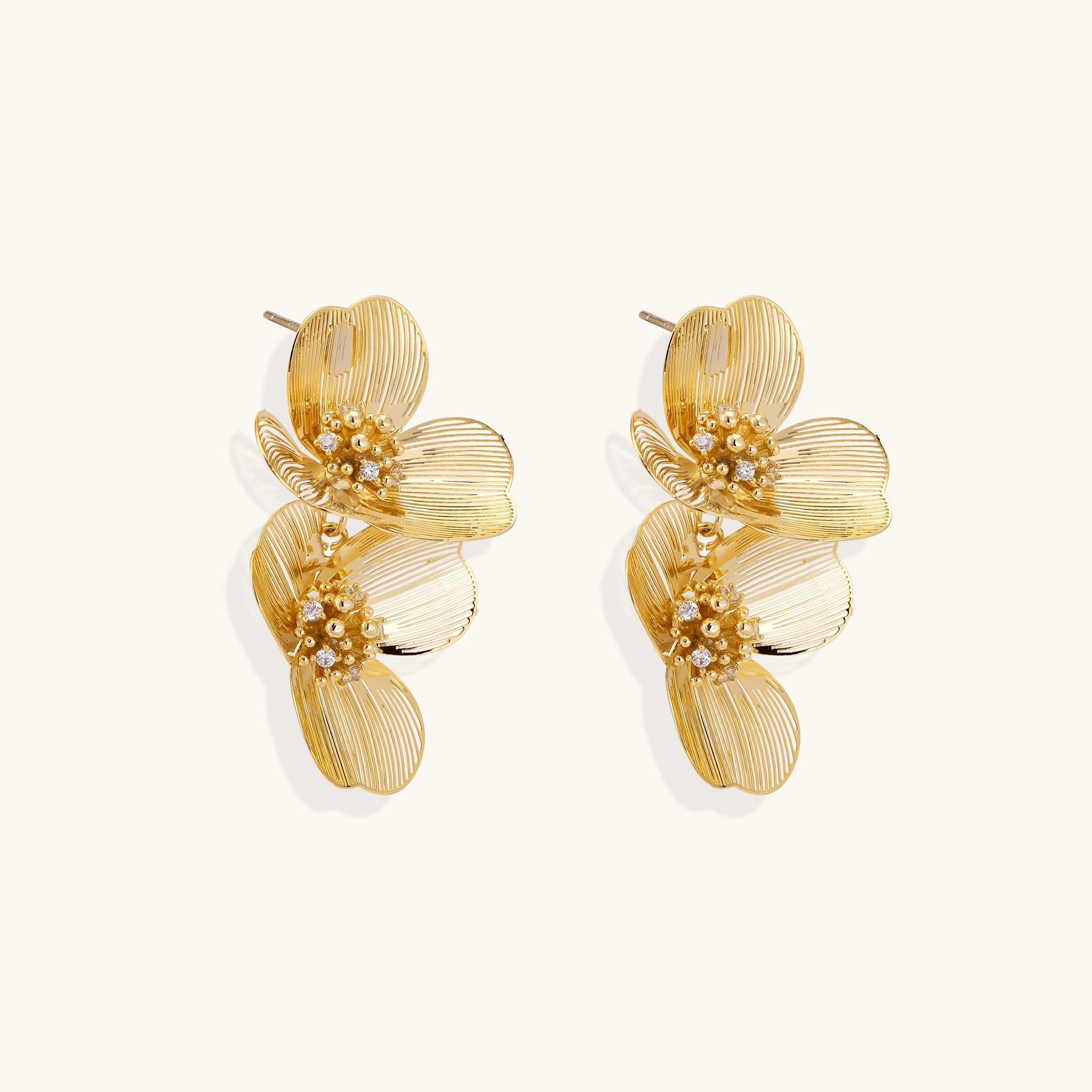 Layered gold-plated floral stud earrings with textured petals and crystal-accented centers on white background.