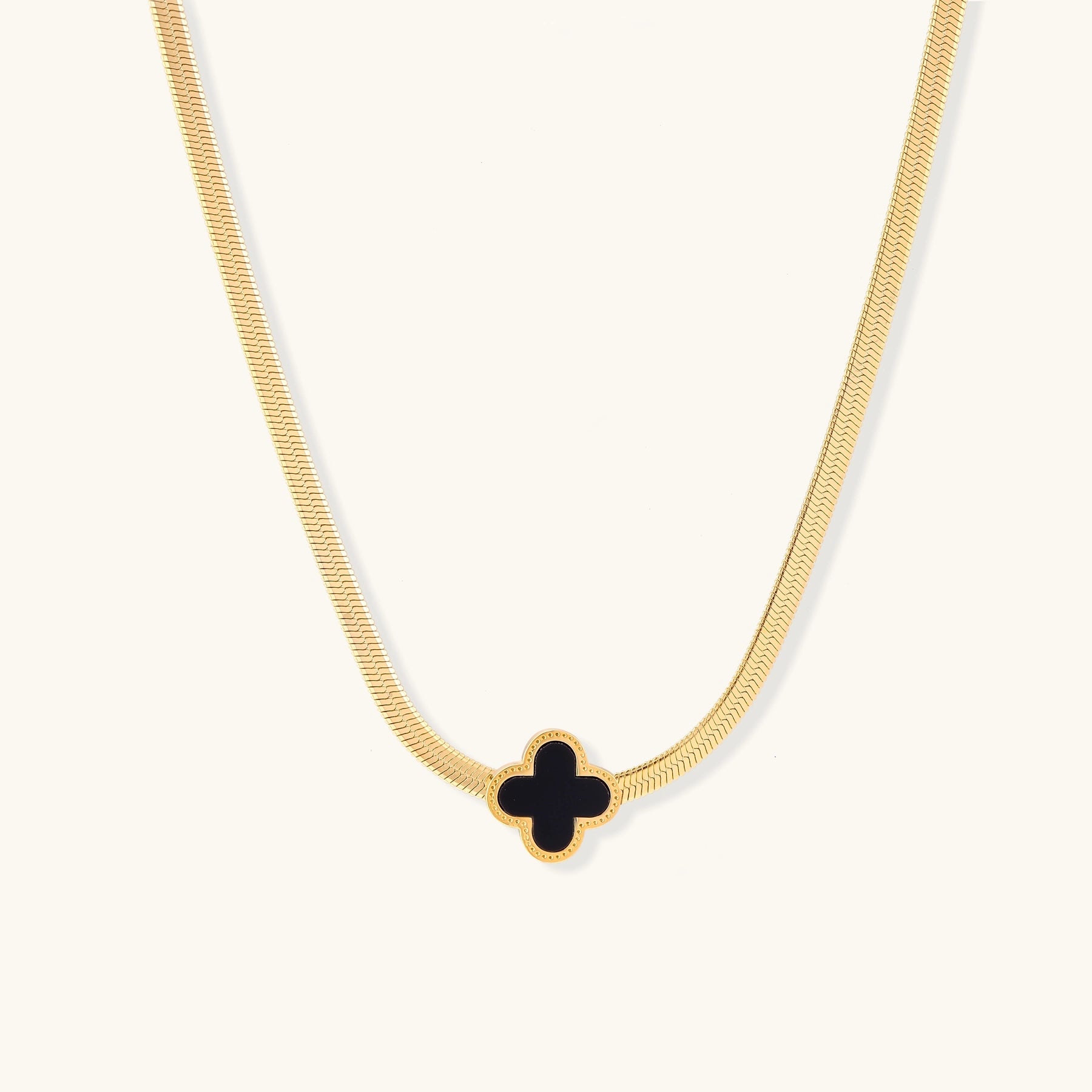 Delicate gold-plated chain necklace featuring a black quatrefoil clover pendant on white background.